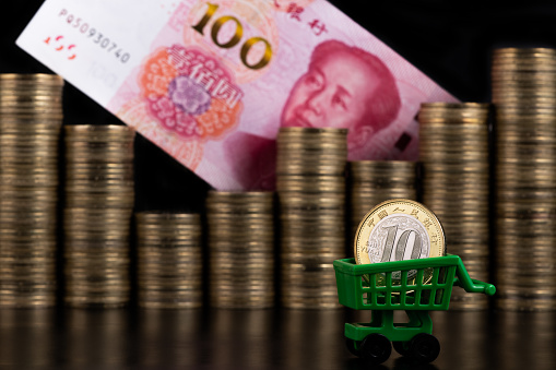 Symbolic story about Chinese currency with 10 yuan denomination, miniature shopping cart and stacked gold coins