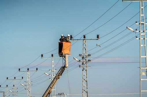 Electrical workers are making a high voltage connection. Electricity poles and cables.