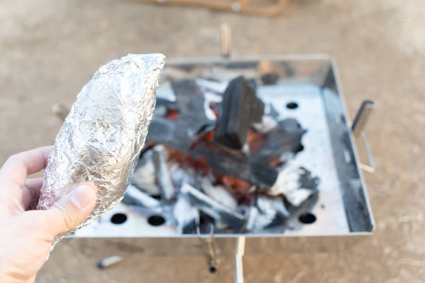 Hand holding potatoes in tinfoil roasted on campfire