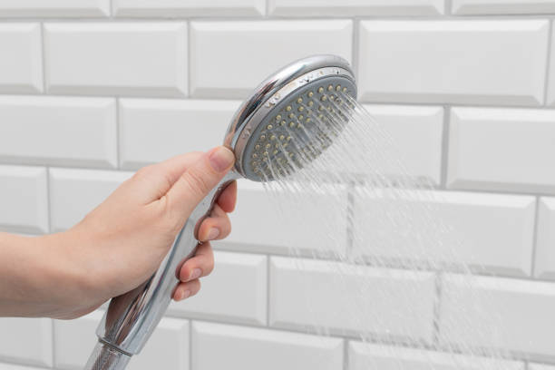 istock Female hands holding a shower head in the bathroom with white brick wall 1466553688