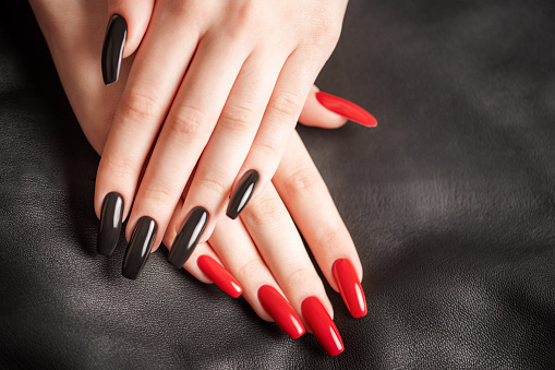 Hands of young girl with black and red manicure on nails on black leather background