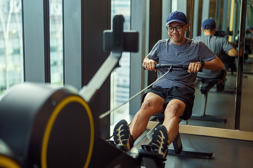 Mid adult Asian man exercising on a rowing machine at the gym. Healthy lifestyle and sport concept
