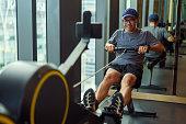 Mid adult Asian man exercising on a rowing machine at the gym