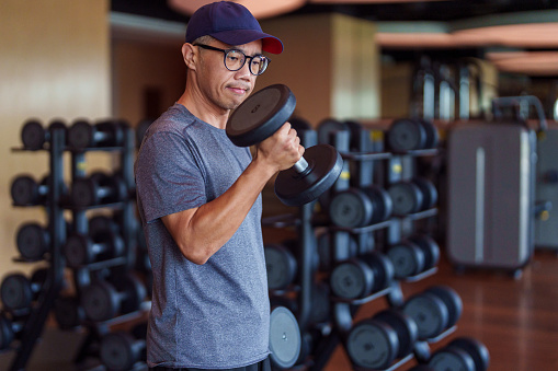 Mid adult Asian man man in sportswear doing an exercise with dumbbells for biceps in a gym club. Healthy lifestyle and sport concept