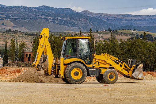 yellow excavator working with mountains in the background