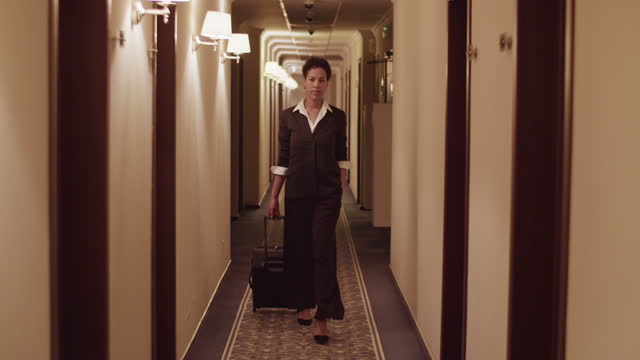Stylish black woman with suitcase walking in hotel hall after check in