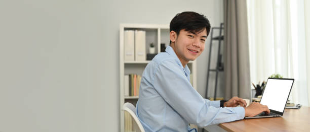 istock Cheerful asian man freelancer using laptop computer in modern home office. Horizontal banner, copy space for text. 1466587365