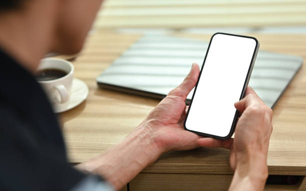 istock Over shoulder view of man using smart phone on wooden desk. Blank screen for advertise text and graphic display montage. 1466587390