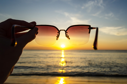 Sunset view through sunglasses in hand, Sunset over the sea, natural background, space for text. The concept of vacation, travel, relaxation and contemplation of beauty