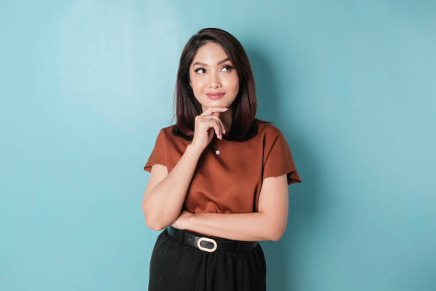 portrait of a thoughtful young casual girl wearing a brown shirt looking aside isolated over blue background - aside imagens e fotografias de stock