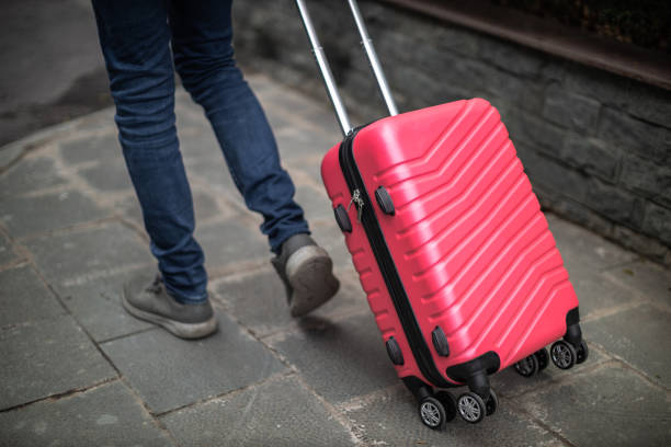 Tourist, wearing a blue jeans,  dirty gray snickers carrying a pink suitcase in Long Bien, Hanoi, Vietnam