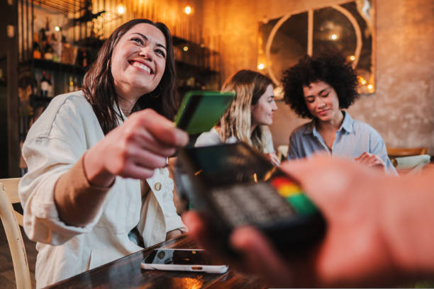 giovane donna felice che paga il conto con una carta di credito contactless in un ristorante. donna sorridente con in mano una carta di credito e che dà una transazione di pagamento al cassiere. - pagare foto e immagini stock