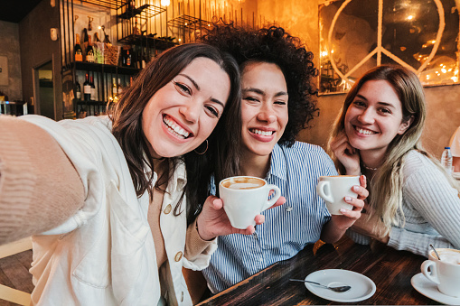 Group of three happy young women taking a selfie portrait on a coffee shop. Multi ethnic friends taking a photo smiling and looking at camera. High quality photo