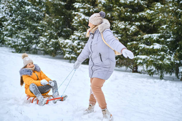 istock Happy mother pulling sledge with kid girl on snowy park road 1466609530