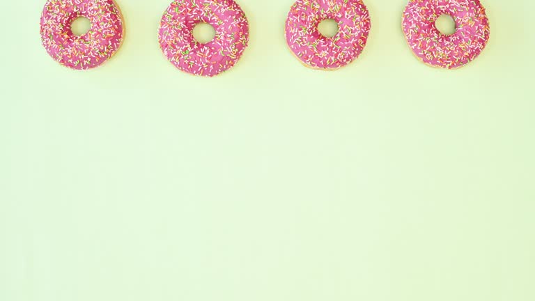 Strawberry glazed donuts spin in circle on top of light green background. Copy space sweet food concept. Stop motion. Flat lay