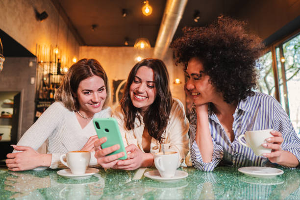 istock Three ladies smiling and having fun using a cellphone to send text messages at restaurant or coffee shop, A group of happy young women laughing using their mobile phone app to share photos. 1466610234