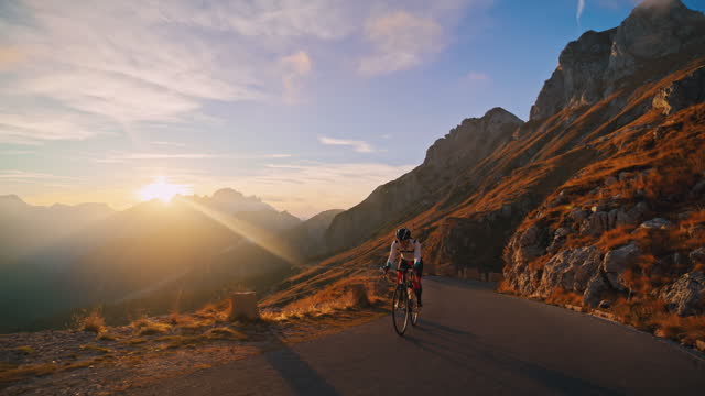 Female cyclist cycling uphill on sunny mountain road at sunrise