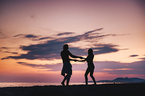 Silhouette of a couple having fun while spinning on the beach at sunset. Copy space.