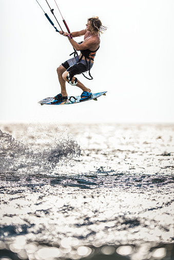 Young athletic man kitesurfing in mid-air during summer day at sea. Copy space.