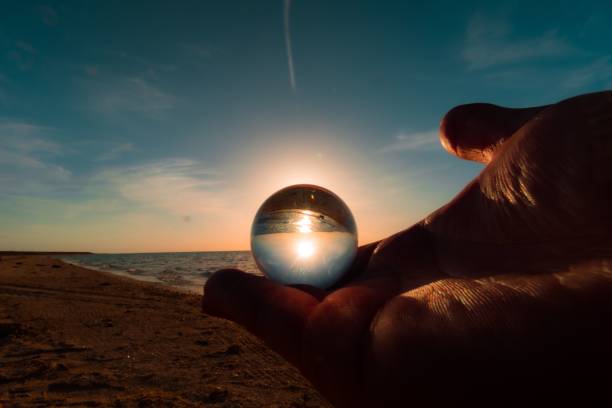 istock Human holding glass sphere with reflection sea during sunset 1466613657