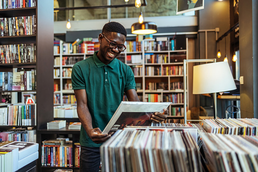 Young man holding the vinyl record disk in the store during the day.