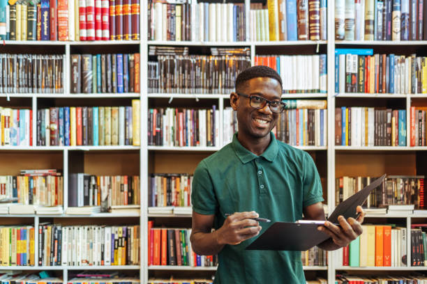 istock African man looking at camera while holding clipboard in bookstore. 1466615149