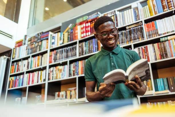 lächelnder männlicher student bei der arbeit in einer bibliothek - male education college student nerd stock-fotos und bilder