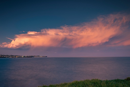 This a photo of a summer reverse sunset storm cloud, moving north along the coast of in Sydney, Australia, with a faint horizontal lightning bolt.