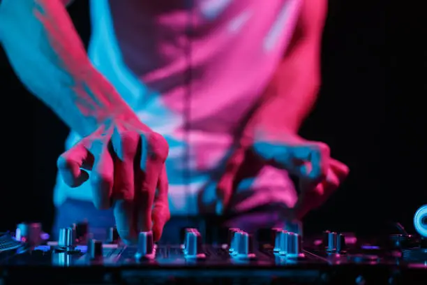 Hands of disc jockey playing electronic music set on stage in night club. Professional audio equipment on techno party