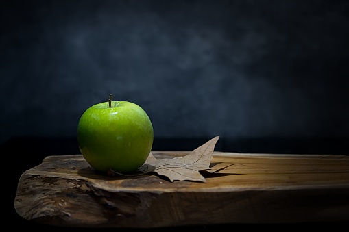 A closeup of a delicious fresh green apple on a wooden table with a dark black background