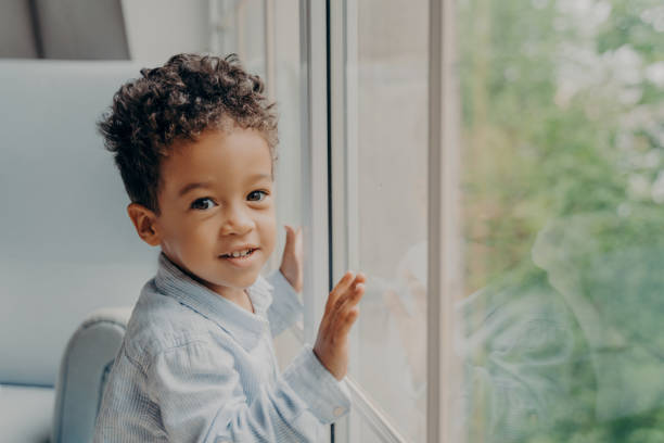 istock Cute mixed race little curly haired boy in light blue colored shirt next to large window 1466624005