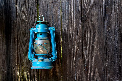 An old blue kerosene lamp hanging on a wooden wall