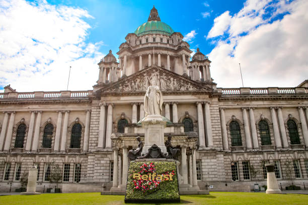 Belfast City Hall building with a classical Renaissance stone exterior and statue in front with a flower arrangement with the word Belfast.  Located in Donegall Square, Belfast, Northern Ireland.