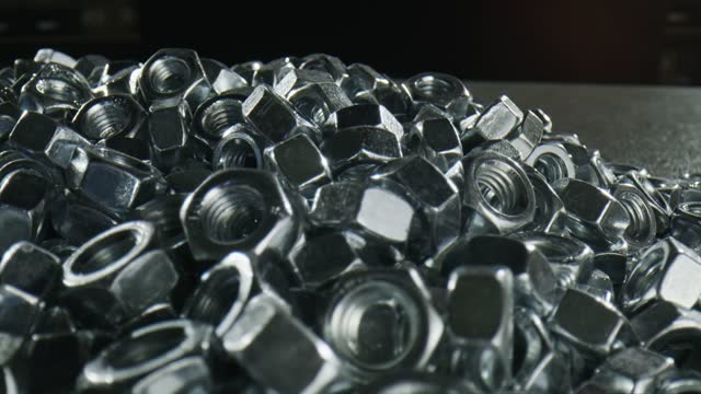 Heap of silver gleaming nuts fasteners on black table