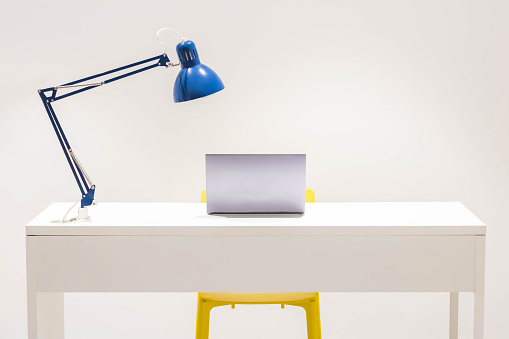 A white desk with blue lamp and yellow chair