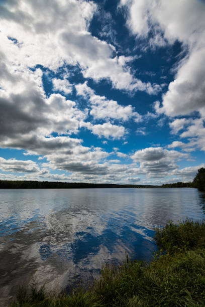 istock Vertical shot of a blue lake under a clouded blue sky with a forest background 1466628212