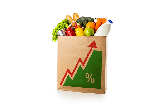 Front view of a shopping bag full of groceries with a red growing arrow and percent sign printed on the side of the bag. The shopping bag is isolated on white background.