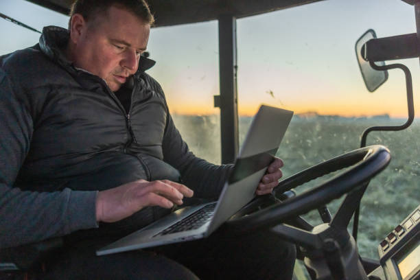 istock Male farmer with short brown hair,sitting inside his tractor,using a laptop 1466633477
