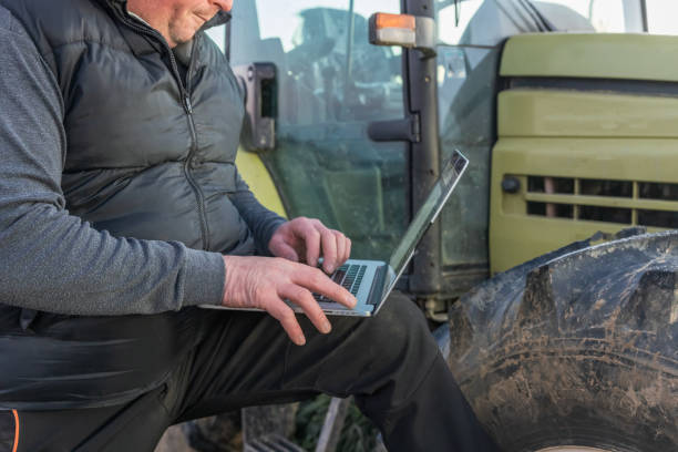 istock Male farmer ,looking down while working on his laptop,standing next to his tractor in the evening 1466634061