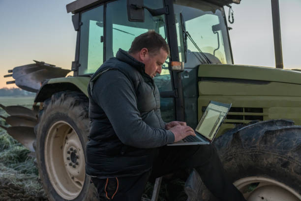 istock Farmer with short brown hair,a using his laptop while standing next to his tractor,leaning his leg up on the wheel,in the evening 1466634103