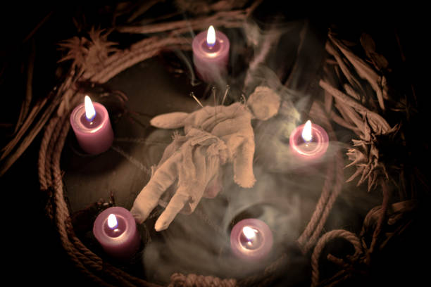 Occultist dripping hot wax on voodoo doll, magic rituals, black spell, horror. stock photo