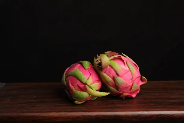 Two fresh dragonfruits on a wooden surface with a background