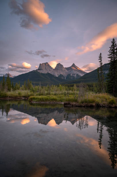 vue des collines verdoyantes et des montagnes rocheuses reflétées sur l’eau au coucher du soleil dans le parc provincial - bow valley photos et images de collection