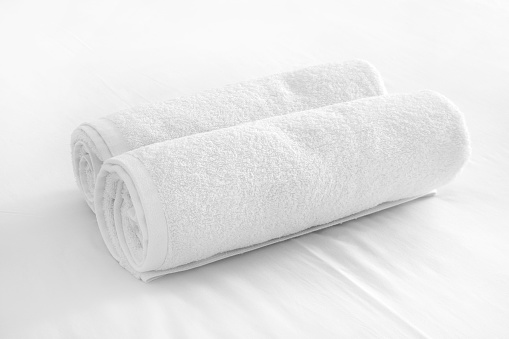 Two white towels formed into a roll are next to each other, on white background