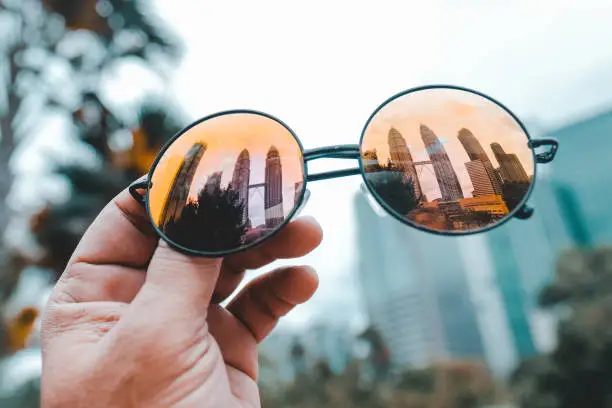 A closeup shot of orange shade sunglasses in a hand reflecting Petronas twin towers in Kuala-Lumpur, Malaysia