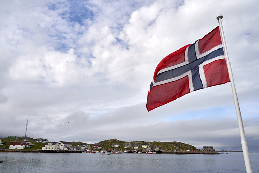 A small northern Norwegian village at the seashore with a national flag in the foreground