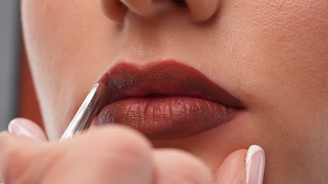 Applying red lipstick on lips close-up.