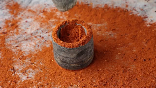 Indian spices hand pounding red chili flakes crushed in stone mortar.