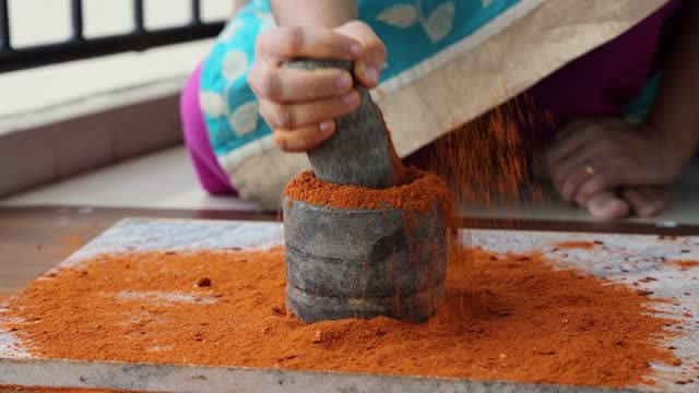 Indian spices hand pounding red chili flakes crushed in stone mortar.