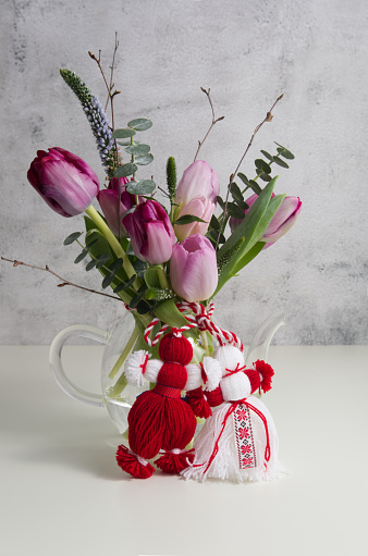 Bouquet of pink and purple tulips tied with red-white martenitsa, martisor on a white table